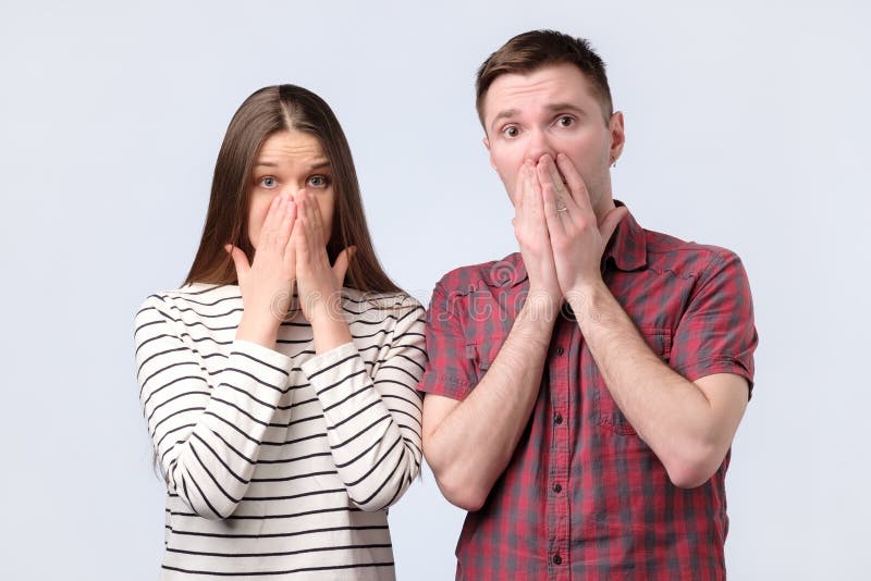 Shocked surpreendeu os pares novos que cobrem a boca com as mãos que olham a câmera fotos de stock Shocked surpreendeu os pares novos que cobrem a boca com as mãos que olham a câmera fotos de stock