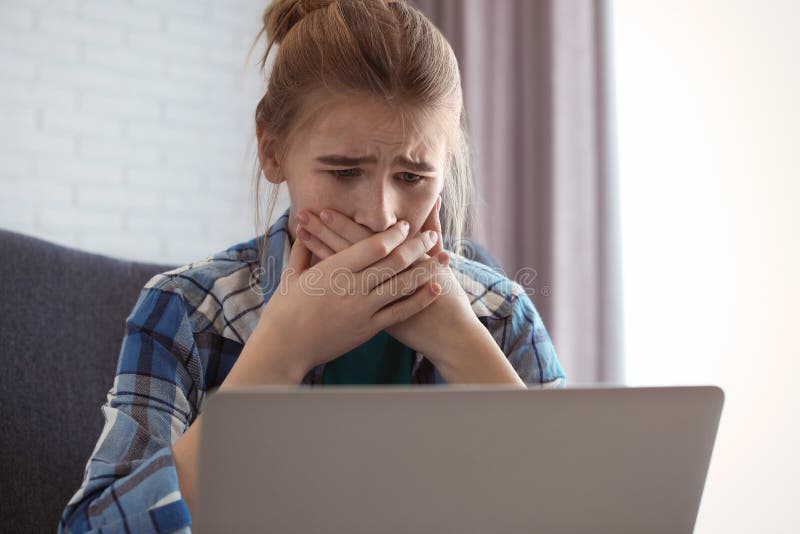 Shocked teenage girl with laptop indoors. Danger of internet