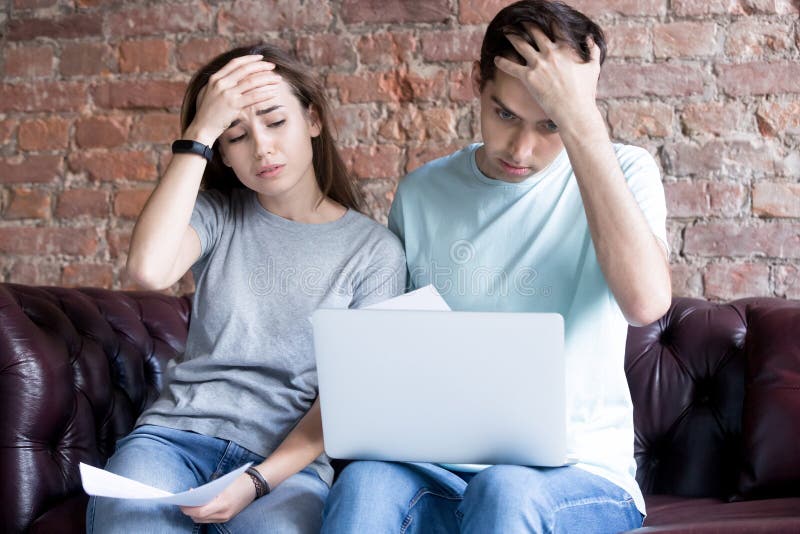 Shocked young couple looking at documents and laptop. stock image
