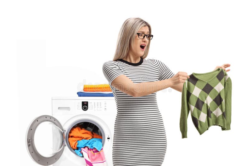 Shocked young woman holding a shrunken blouse in front of washing machine