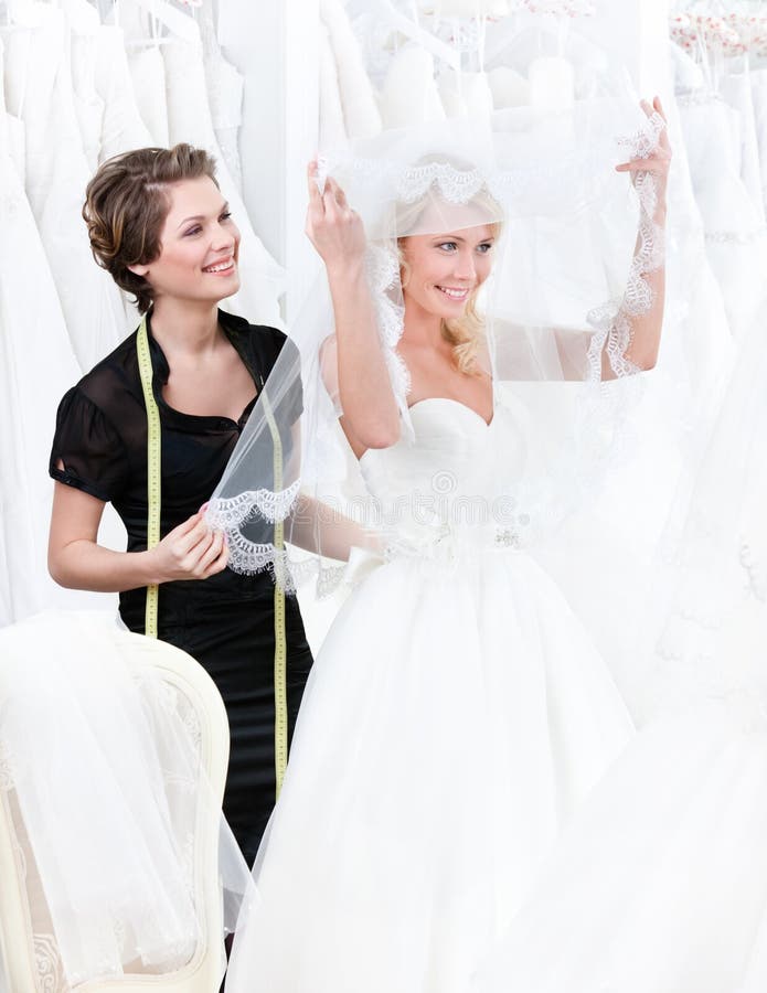 Shop assistant helps to the bride to put the weddi