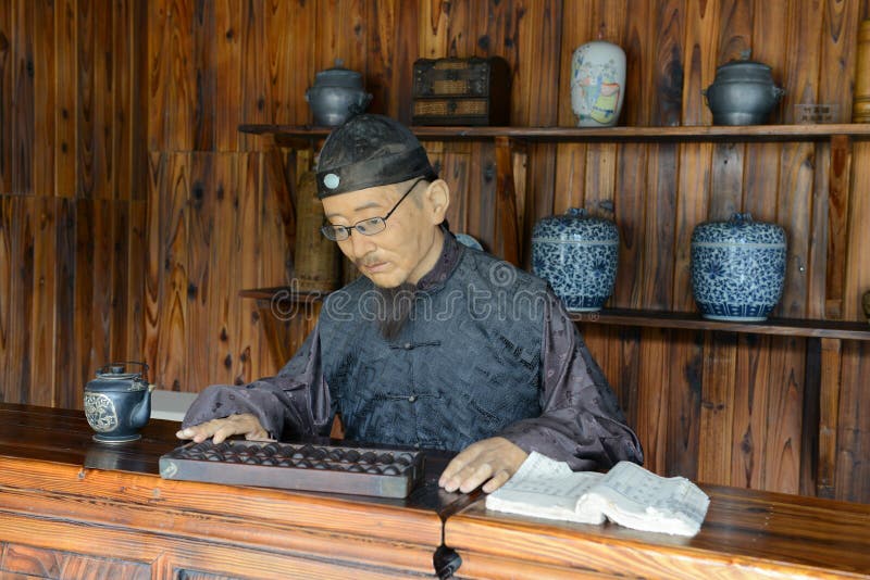 Shopkeeper of a Tea house in ancient China. He uses a Abacus, the ancient Chinese adding machine which uses beads for counting to check the account book. The shopkeeper in this image is made of wax.