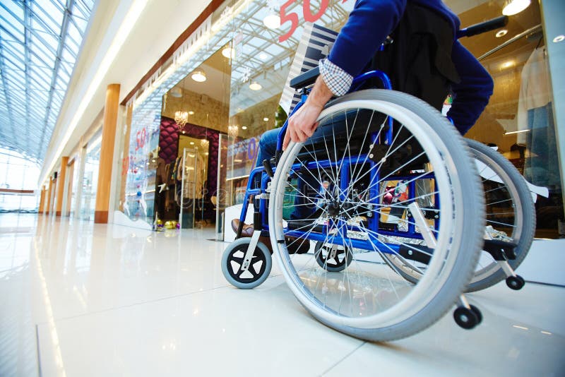 Disabled shopper moving in wheelchair along departments in the mall. Disabled shopper moving in wheelchair along departments in the mall