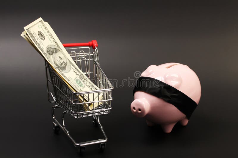 Shopping basket with stack of money american hundred dollar bills inside and pink piggy bank with black blindfold standing