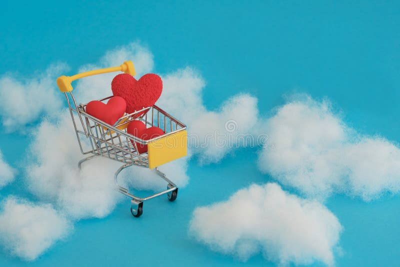 Shopping dream with love. Yellow shopping cart with red hearts inside on a blue background and clouds. Valentine`s day. Shopping dream with love. Yellow shopping cart with red hearts inside on a blue background and clouds. Valentine`s day