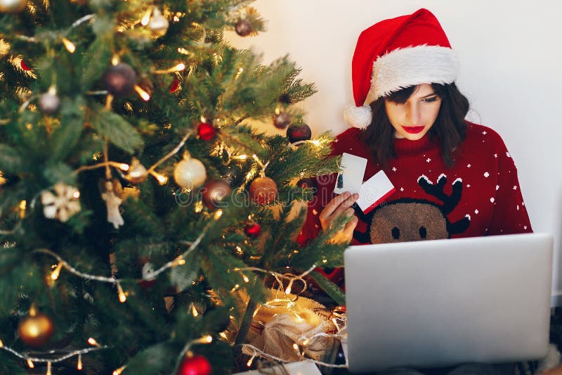 shopping online and christmas sale concept. stylish woman in reindeer hat holding credit card and laptop, under christmas tree li