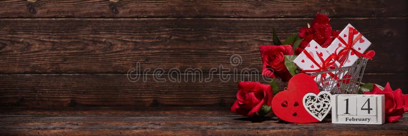 Shopping trolley, gifts, hearts on brown wooden background. 14 February. Valentine`s Day. Extra wide panorama banner background