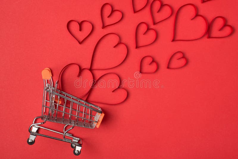 Shopping on Valentines Day concept idea. Flat lay close up view photo of empty push cart and flying blowing away red hearts isolated bright background.