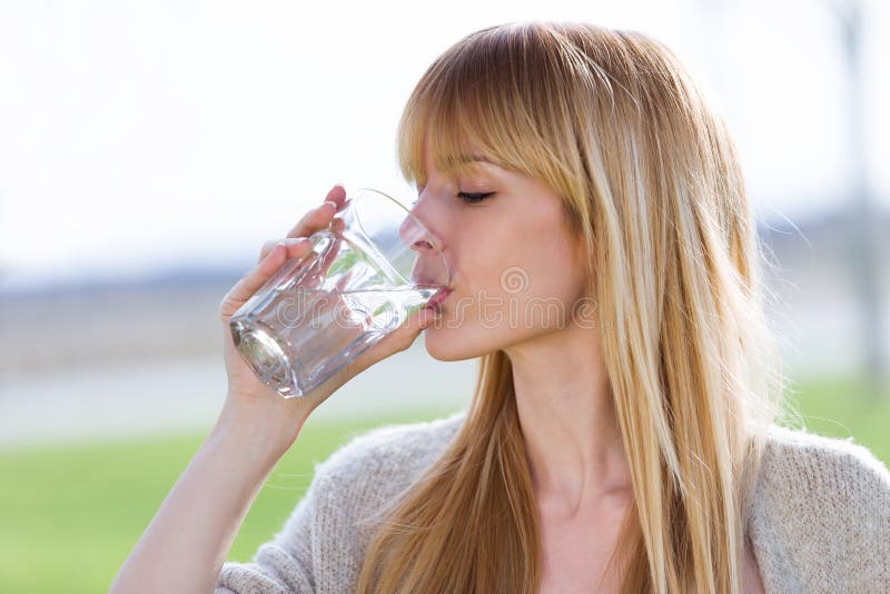 Beautiful young woman drinking water glass in the park.