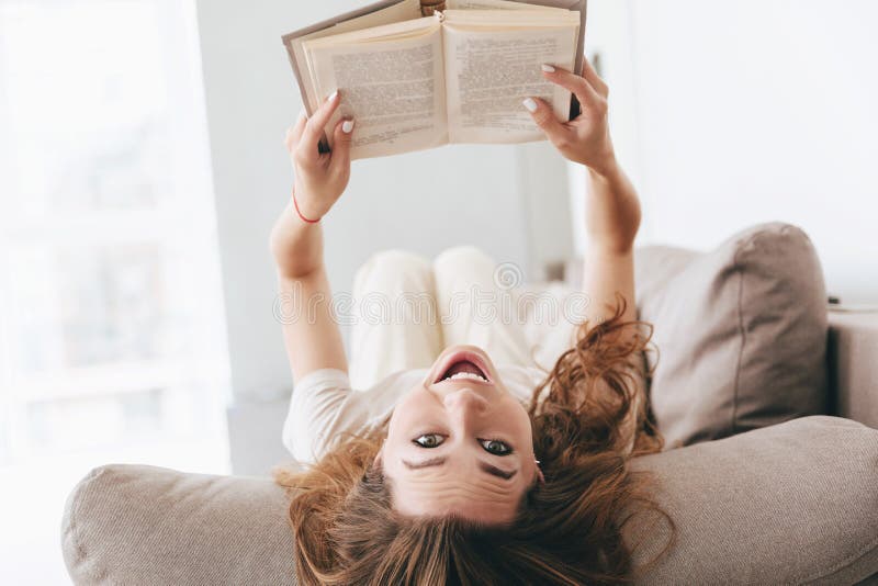 Shot of funny woman lying on couch with book