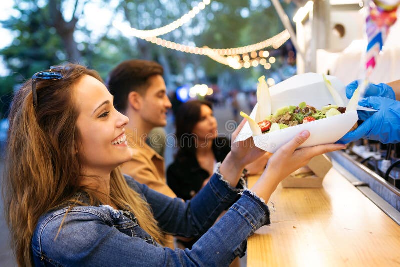 Group of attractive young friends choosing and buying different types of fast food in eat market in the street. royalty free stock photo