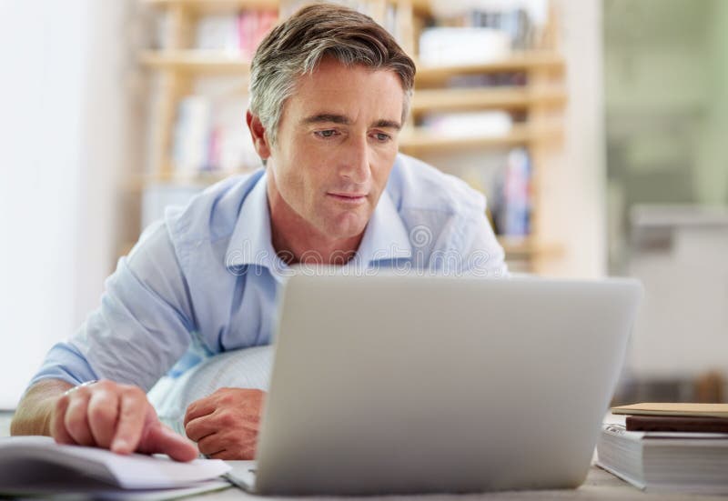 Comparing Notes Shot Of A Handsome Mature Man Lying On His Living Room Floor Using A Laptop