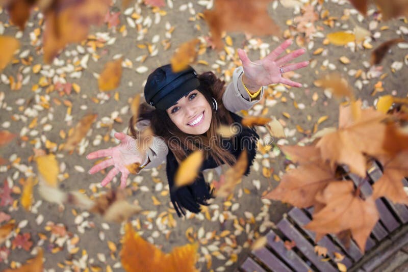 Pretty young woman looking to the sky with arms raised as leaves fall from the trees in the park in autumn stock image Pretty young woman looking to the sky with arms raised as leaves fall from the trees in the park in autumn stock image