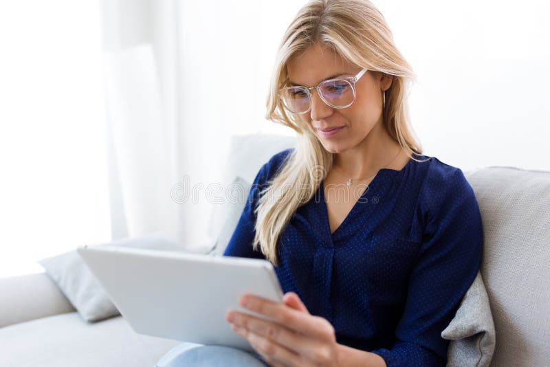 Smiling young woman using her digital tablet while sitting on sofa at home.