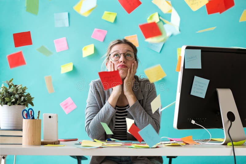 Stressed young business woman looking up surrounded by post-its in the office