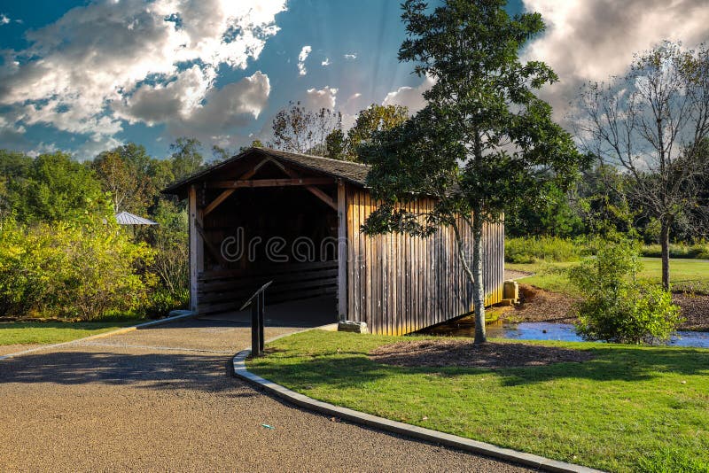 A shot of a wooden covered bridge over a river surrounded by lush green and autumn colored trees with lush green grass