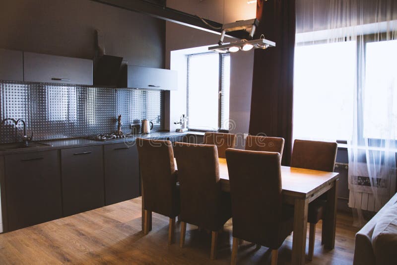 Shot of a wooden table with wooden chairs near window curtains in a kitchen with black interior royalty free stock image Shot of a wooden table with wooden chairs near window curtains in a kitchen with black interior royalty free stock image