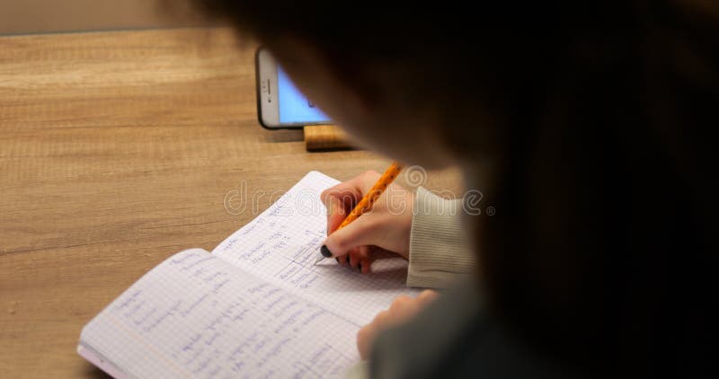 Shoulder shot of teenager use smartphone write down notes to notebook royalty free stock photo