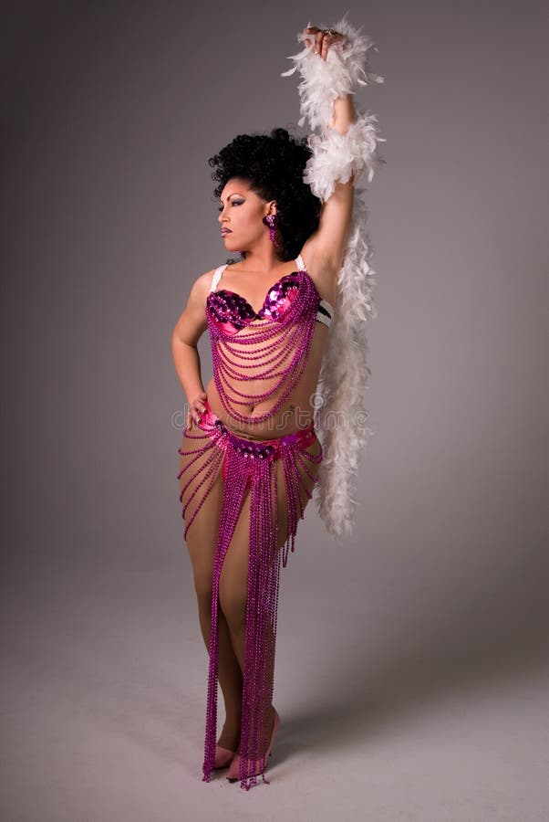 Full length shot of a glamorous Drag queen wearing a pink beaded showgirl costume, with a white feather boa wrapped around her arm.