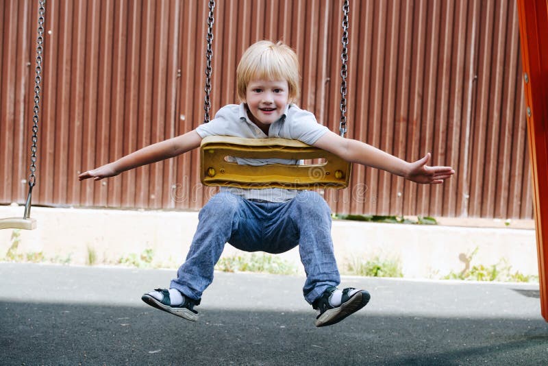 Showing off little boy riding on swings on his stomach at a children playground.