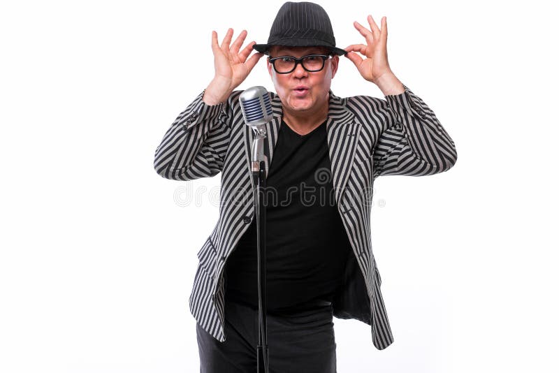 Showman śpiew w mikrofonie z emocjonalnym gestem. Charyzmatyczny przystojny mężczyzna w kostiumu z czarnym kapeluszem i mikrofonem possing na białym tle
