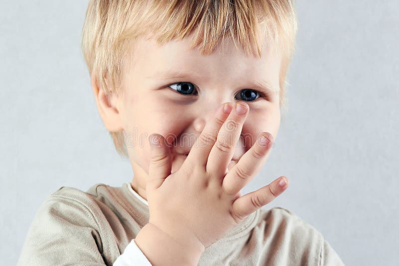 Shy blond boy hide his nose and mouth with hid hand stock photo