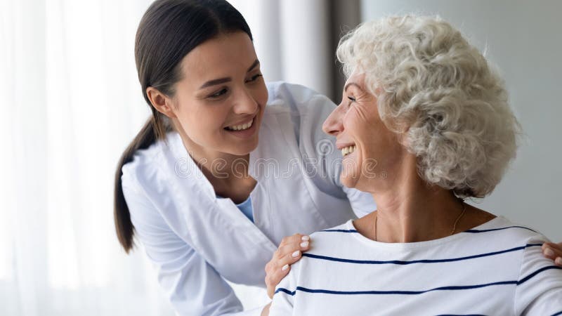 Si prende cura di una giovane infermiera sorridente che si prende cura della nonna anziana. fotografia stock libera da diritti