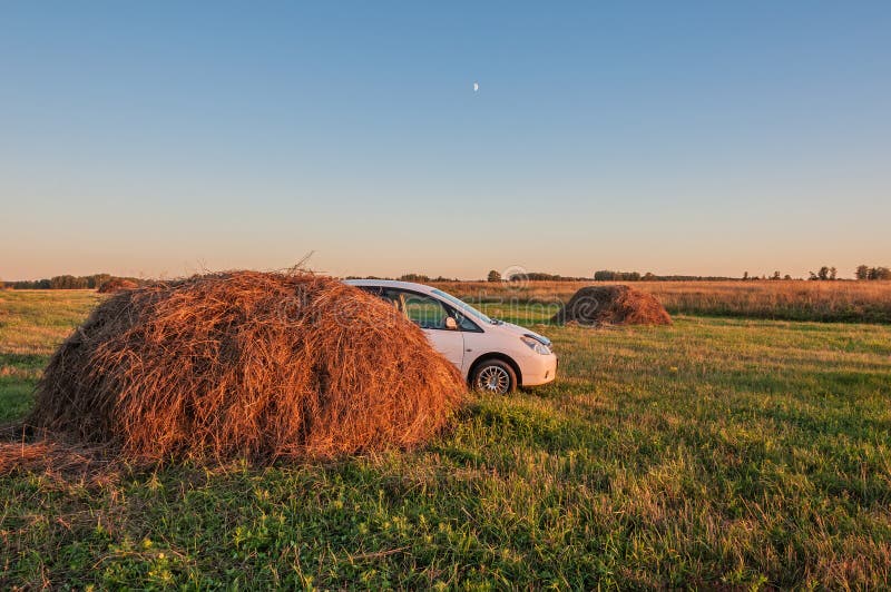 Rural landscape with haystacks and a white car in the evening light. Rural landscape with haystacks and a white car in the evening light