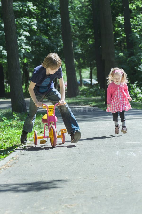 Sibling children are happy playing tag game by running and riding kids tricycle