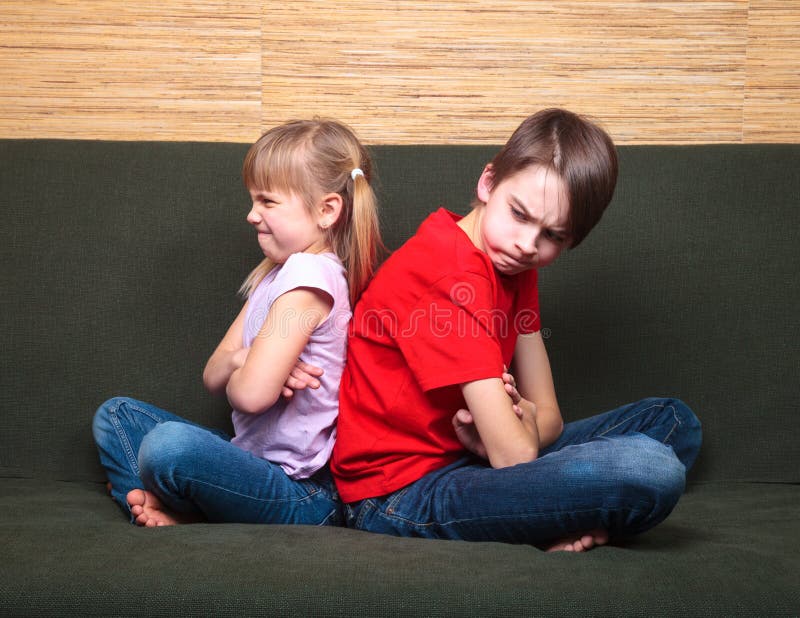 Brother and sister wearing casual clothes sitting on a green sofa at home arms crossed back to back angry with each other. Brother and sister wearing casual clothes sitting on a green sofa at home arms crossed back to back angry with each other