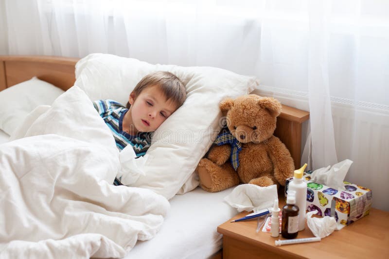 Enfermo chico acostada en una cama fiebre, está descansando sobre el.