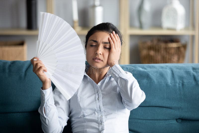 Sick indian girl feel unwell suffer from heatstroke. Unwell sick millennial Indian woman sit on couch wave with hand fan breathe fresh air, overheated young royalty free stock image Sick indian girl feel unwell suffer from heatstroke. Unwell sick millennial Indian woman sit on couch wave with hand fan breathe fresh air, overheated young royalty free stock image