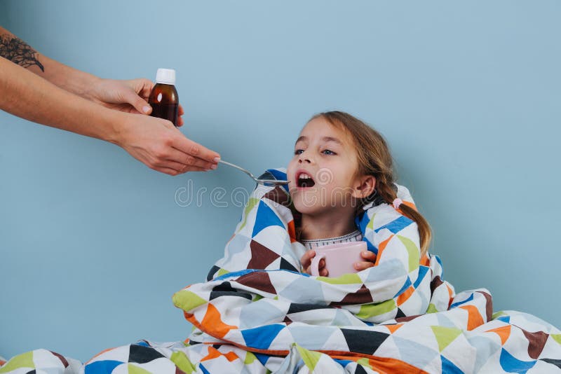 Sick little girl with common cold is sitting in bed, taking medicine