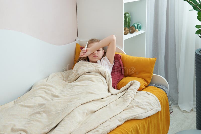 Sick preteen girl laying in bed using thermometer stock images