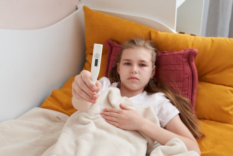 Sick preteen girl laying in bed using thermometer royalty free stock photography