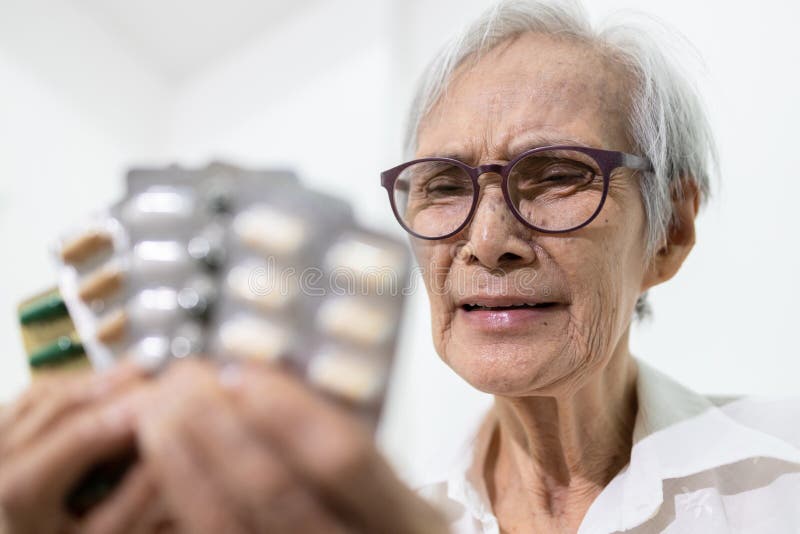 Sick senior woman holding medicine pills or capsules,sad female elderly showing a lot of drugs,treatment,medication to reduce pain