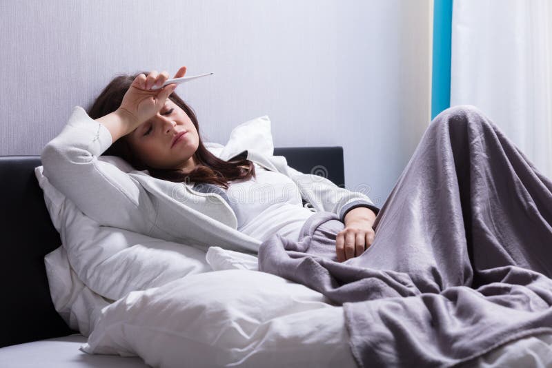 Sick Woman Lying On Bed Holding Thermometer royalty free stock photo.
