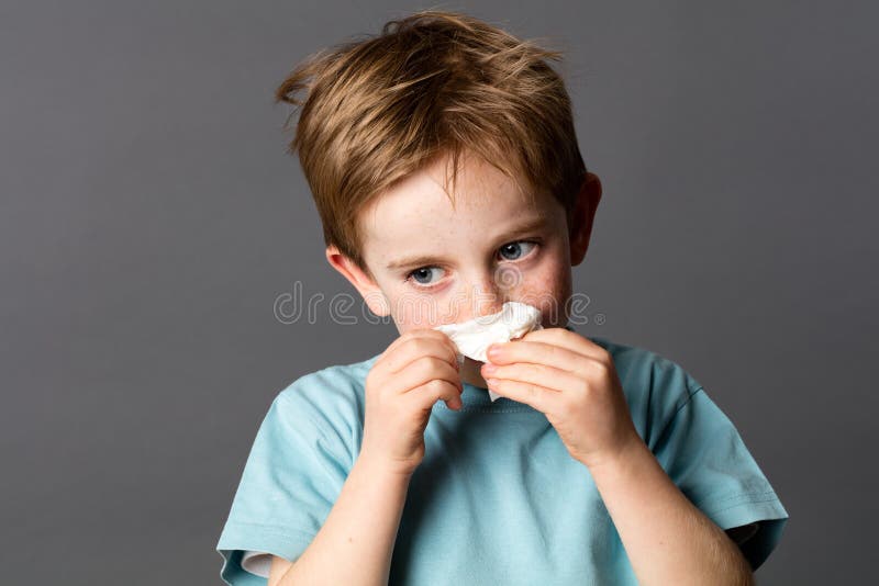 Sick young kid using a tissue after cold or spring allergies
