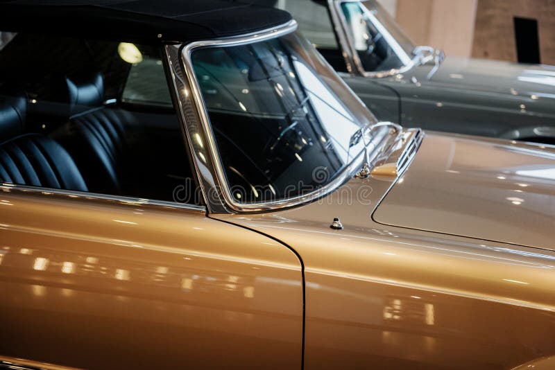 Side, lose up view of beige retro cabriolet car with black roof, steering wheel, chrome window trim and windshield