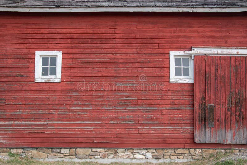 Side of an old red barn with white framed square windows and sliding door