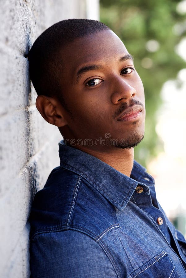 Side portrait of handsome young black man leaning on wall outside