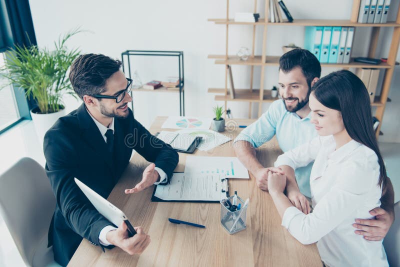 Side profile high angle shot of a deal between married couple and a salesman, consultating them about buying a purchase, all are dressed in formal outfits, smiling