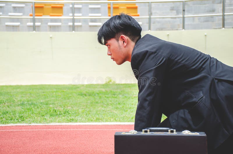 Side view of Asian business man ready to run on the lanes of a track royalty free stock image