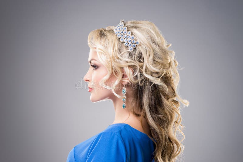 Side view of beautiful, young lady wearing sapphire coronet and earrings over grey background