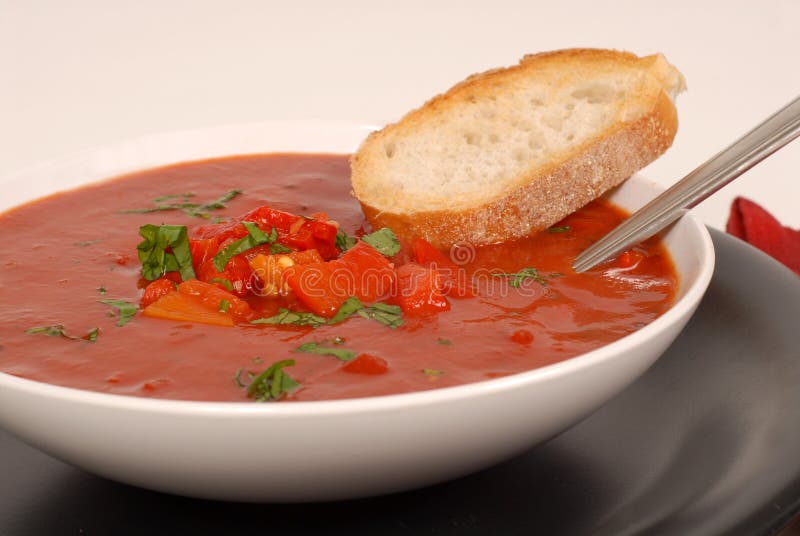 Side view of a bowl of tomato, red pepper and basil soup with br