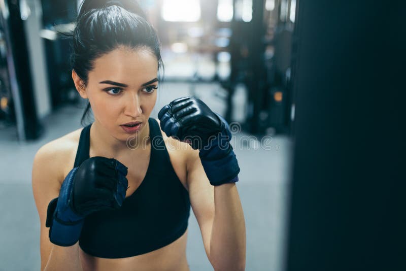 Side view of boxing attractive brunette woman punching a bag with kickboxing gloves in the gym workout. Sport, fitness, lifestyle royalty free stock images Side view of boxing attractive brunette woman punching a bag with kickboxing gloves in the gym workout. Sport, fitness, lifestyle royalty free stock images
