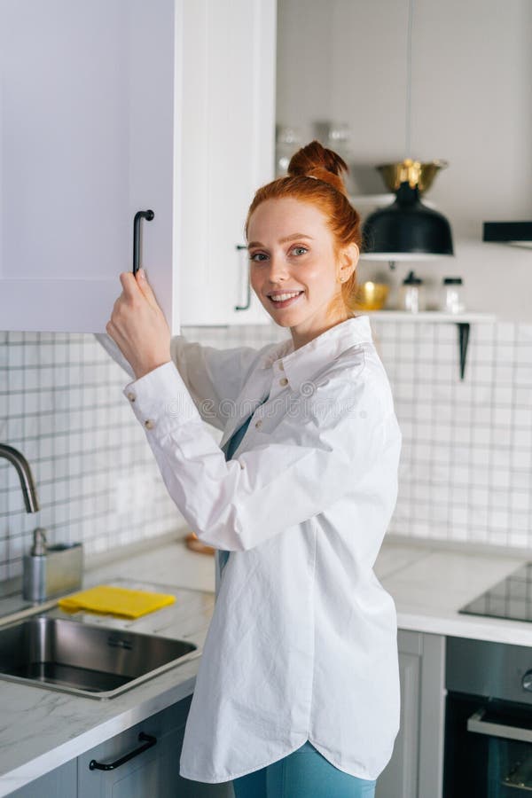 Side View Of Cheerful Redhead Young Woman Opening Door Of Kitchen 