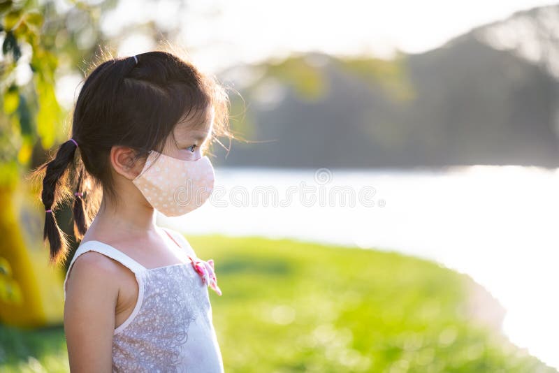 Side view of cute kid girl wearing cloth face mask was standing in park in evening. During summer or spring. Relax time.