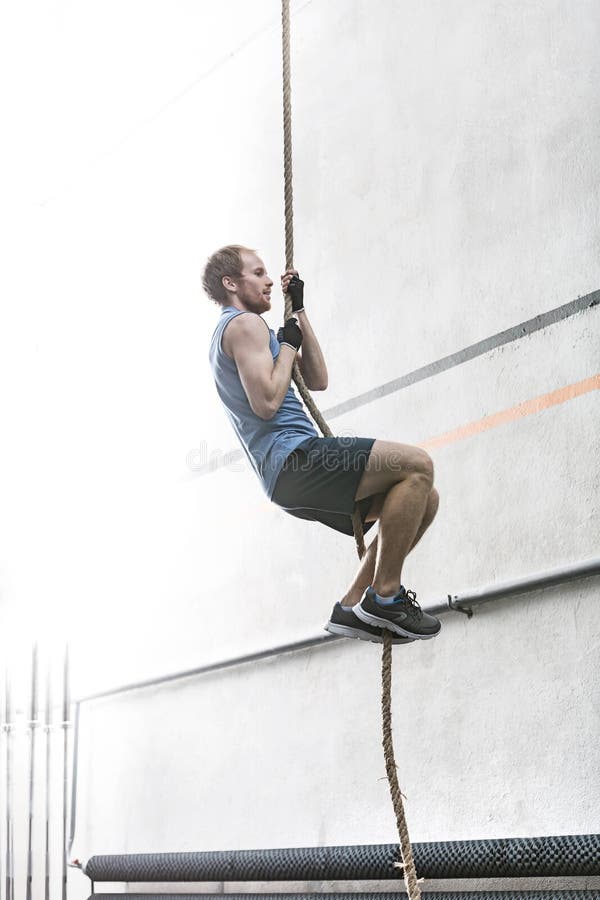 Side View of Determined Man Climbing Rope in Crossfit Gym Stock