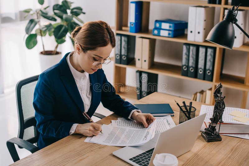 Side View of Female Lawyer Doing Paperwork at Workplace with Laptop